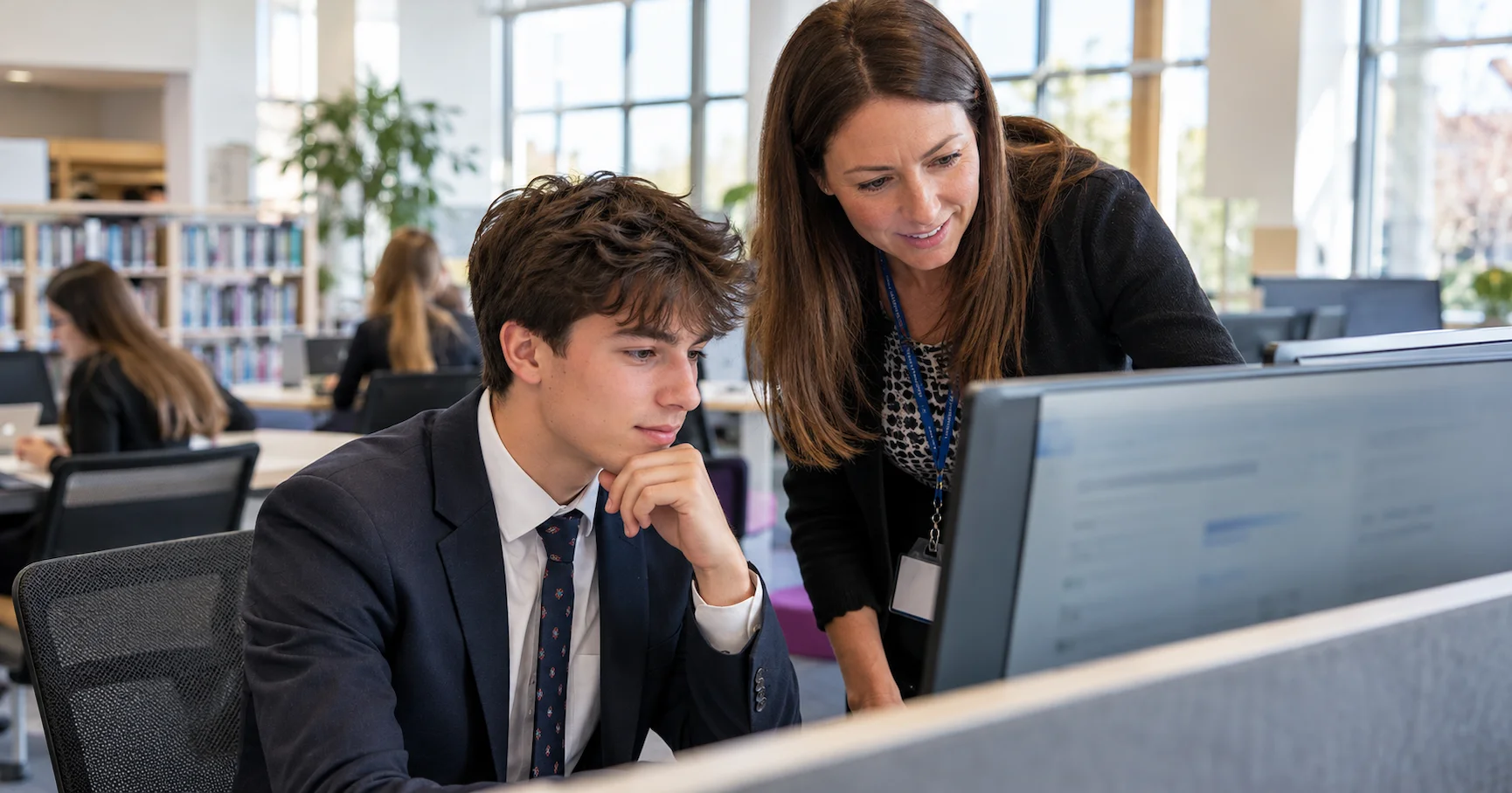 A Year 13 student working on a UCAS university application at a school computer in an English sixth form centre, with a teacher providing support